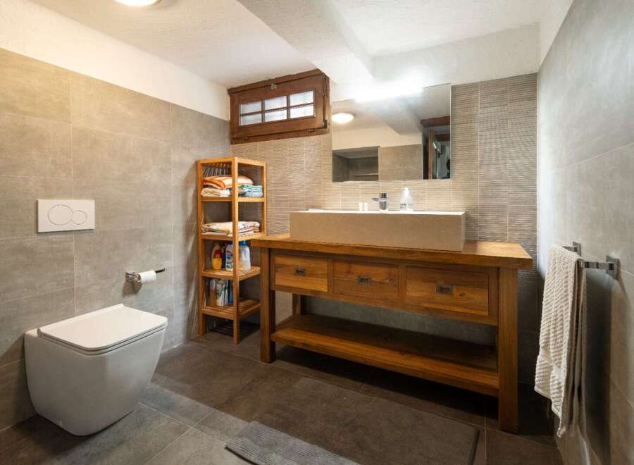 This modern bathroom features sleek gray tiling, a rustic wooden vanity with a stone sink, and open shelving for storage.