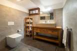 This modern bathroom features sleek gray tiling, a rustic wooden vanity with a stone sink, and open shelving for storage.