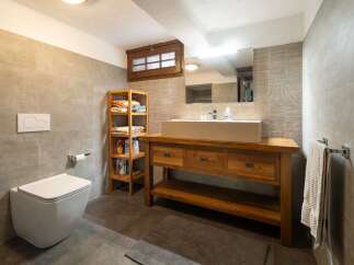 This modern bathroom features sleek gray tiling, a rustic wooden vanity with a stone sink, and open shelving for storage.