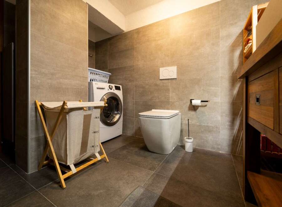 This is a modern bathroom featuring a washing machine, a toilet, and a wooden vanity.