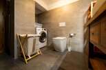 This is a modern bathroom featuring a washing machine, a toilet, and a wooden vanity.