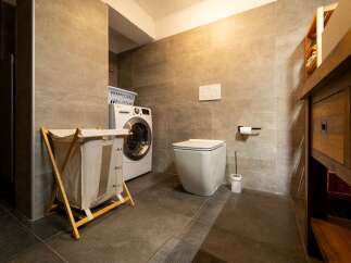 This is a modern bathroom featuring a washing machine, a toilet, and a wooden vanity.