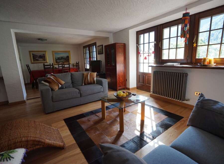 This inviting living room features a comfortable gray sofa, a glass-topped coffee table on a stylish patchwork rug, and large windows offering scenic mountain views.