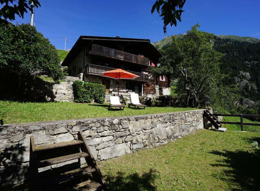 Escape to this charming Swiss chalet nestled in the mountains, boasting a stone facade and multiple balconies.