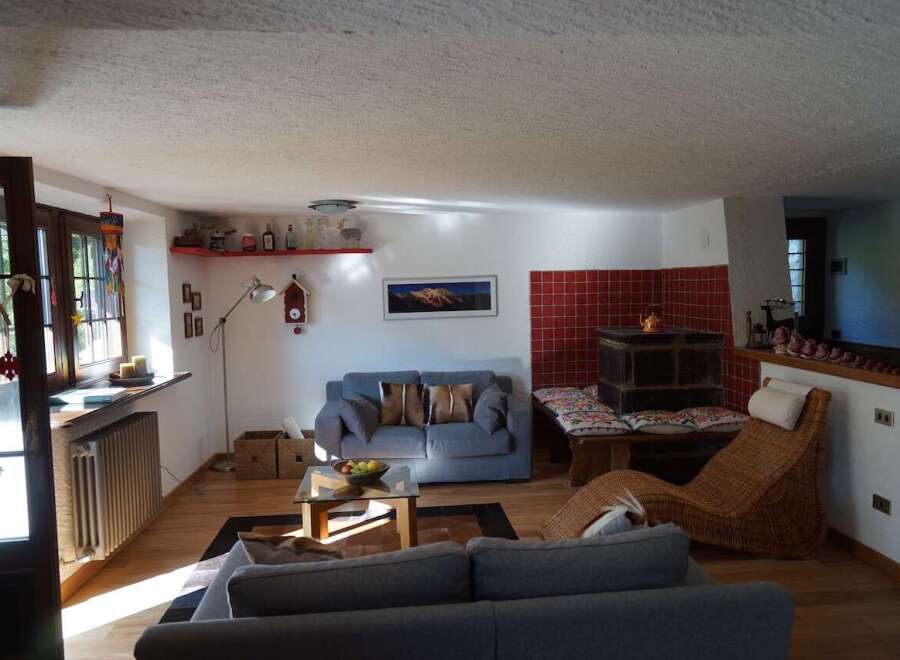 This cozy living room features hardwood floors, white walls, and a comfortable seating area with couches and a wicker chaise lounge.