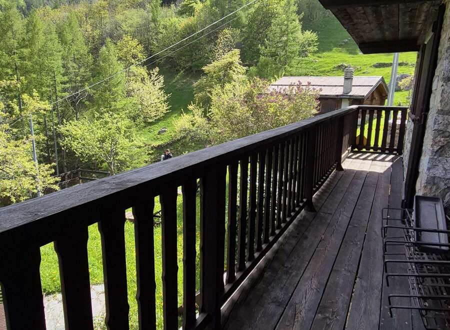 Escape to tranquility with this charming property featuring a wooden balcony overlooking a lush green landscape.