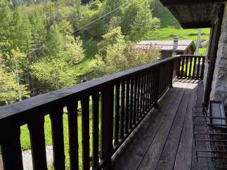 Escape to tranquility with this charming property featuring a wooden balcony overlooking a lush green landscape.