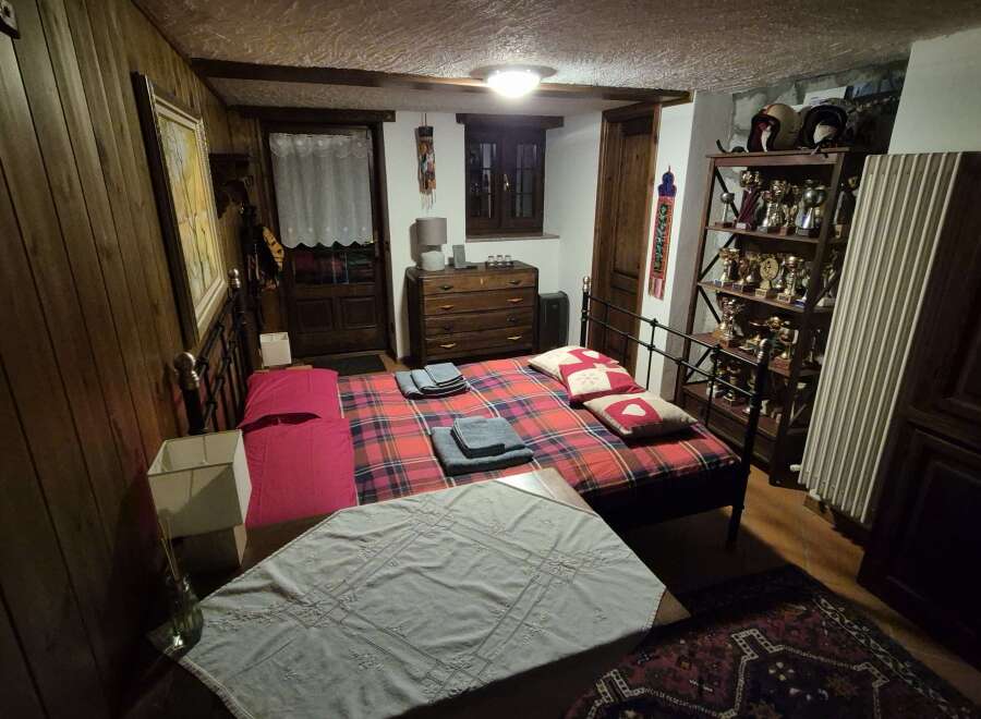 This cozy bedroom features rustic wood paneling, a comfortable plaid bed, and antique furnishings, creating a warm and inviting atmosphere.