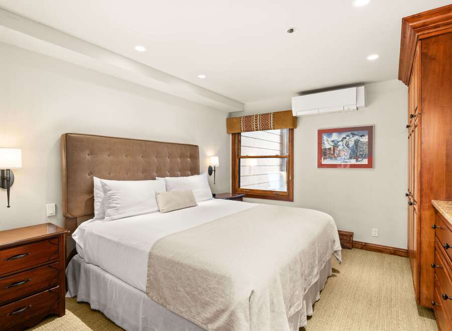This bedroom features a king-size bed with a padded headboard, bedside tables with lamps, and a built-in wardrobe.