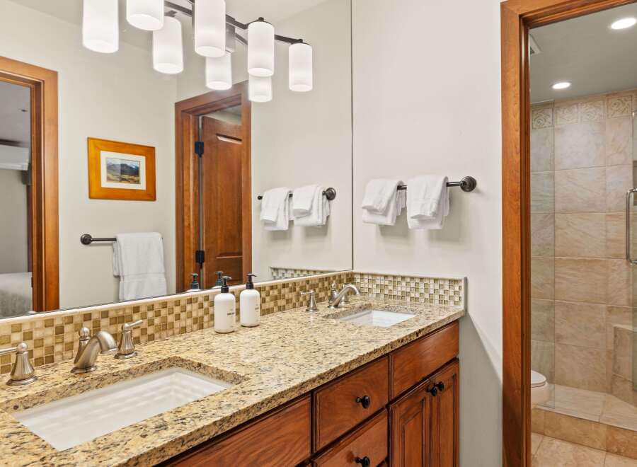 This bathroom boasts a double vanity with granite countertops and mosaic tile backsplash, providing both style and functionality.
