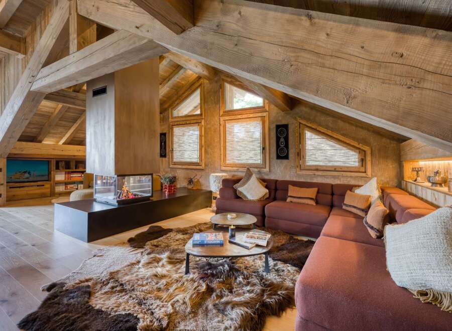 Discover this luxurious chalet featuring exposed wooden beams, a modern fireplace, and cozy sectional seating.
