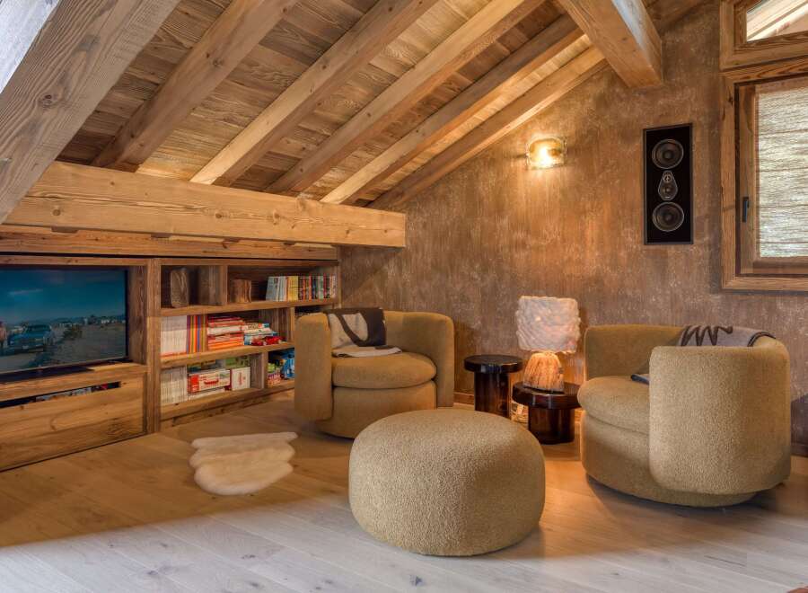 This inviting attic space is designed as a cozy retreat, featuring exposed wooden beams and built-in wooden shelving.