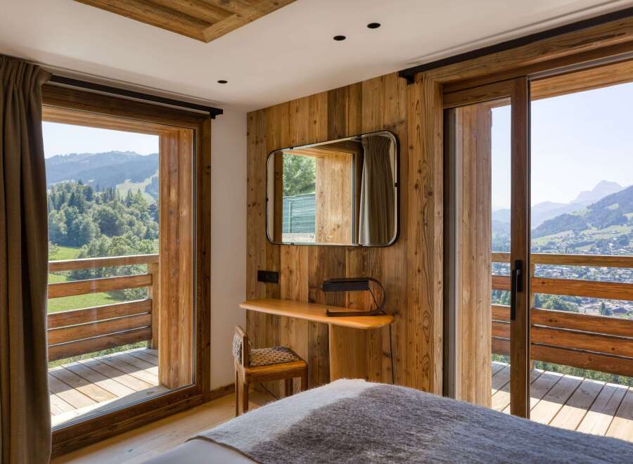 Experience mountain living in this charming bedroom featuring wood paneling, a built-in desk, and a private balcony.