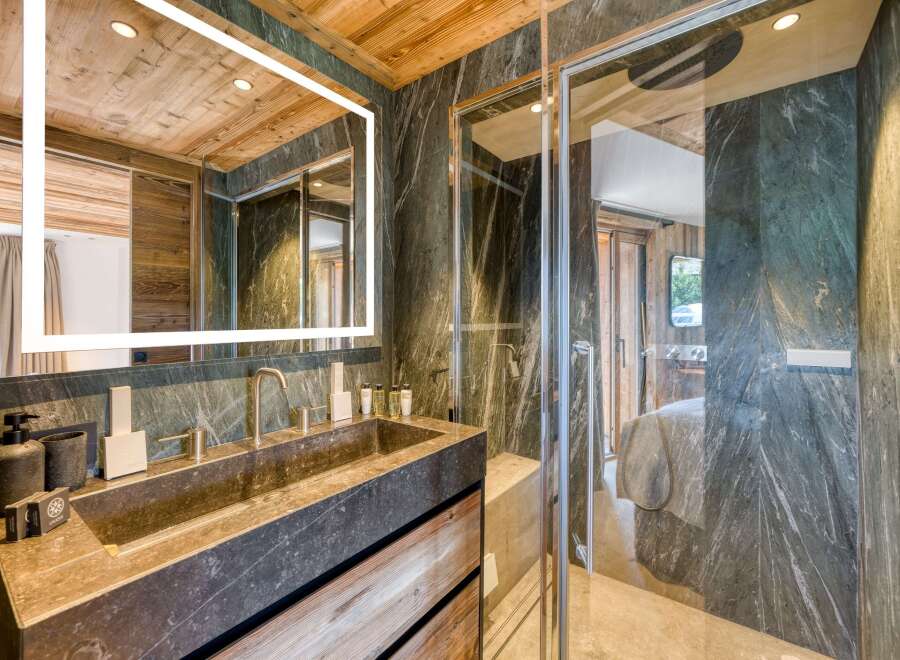 This bathroom features a stunning stone sink and shower with matching stone walls, complemented by warm wood accents on the ceiling and vanity.