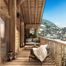 A luxurious chalet balcony offers stunning mountain views, inviting seating, and rustic wooden architecture.