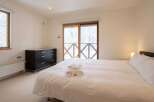 Experience cozy comfort in this inviting bedroom featuring a plush bed with fresh towels, a dark wood dresser for ample storage, and a window offering picturesque winter views.