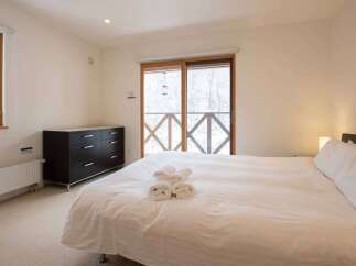 Experience cozy comfort in this inviting bedroom featuring a plush bed with fresh towels, a dark wood dresser for ample storage, and a window offering picturesque winter views.