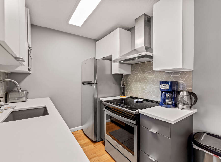 This modern kitchen features sleek white cabinets, stainless steel appliances, and a stylish geometric backsplash.