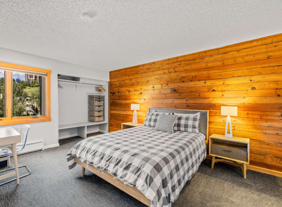Discover a cozy bedroom featuring a striking wood-paneled wall, a comfortable bed with a stylish gray and white checkered duvet, and functional built-in closet space.