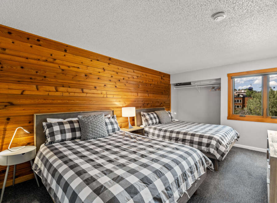 This inviting bedroom features two queen beds with stylish black and white checkered bedding, complemented by a warm wood-paneled wall.