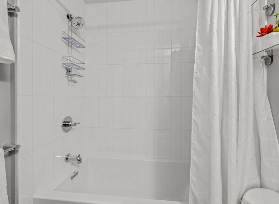 This bathroom showcases a pristine white tiled shower and tub combination, complemented by sleek chrome fixtures.