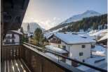 A scenic view from a wooden balcony showcases snow-covered buildings nestled in a mountain village.