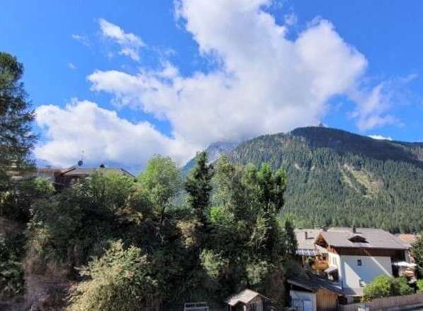 Nestled in a serene mountain landscape, this charming property boasts breathtaking views of lush forests and a clear blue sky dotted with clouds.