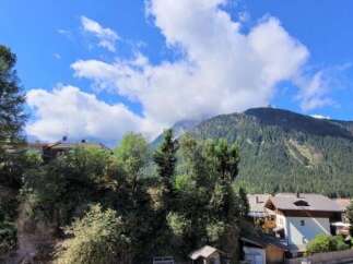 Nestled in a serene mountain landscape, this charming property boasts breathtaking views of lush forests and a clear blue sky dotted with clouds.