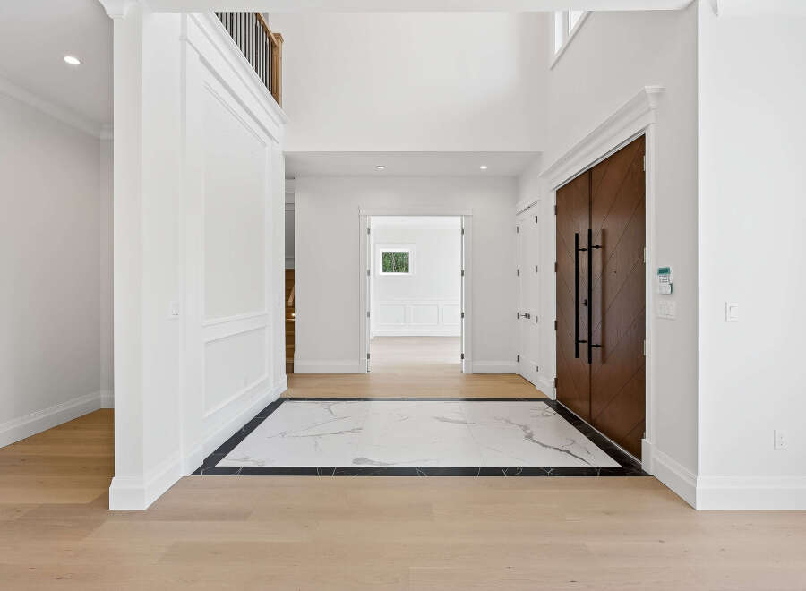 This grand foyer features a striking combination of materials, blending warm wood floors with a chic marble inlay.