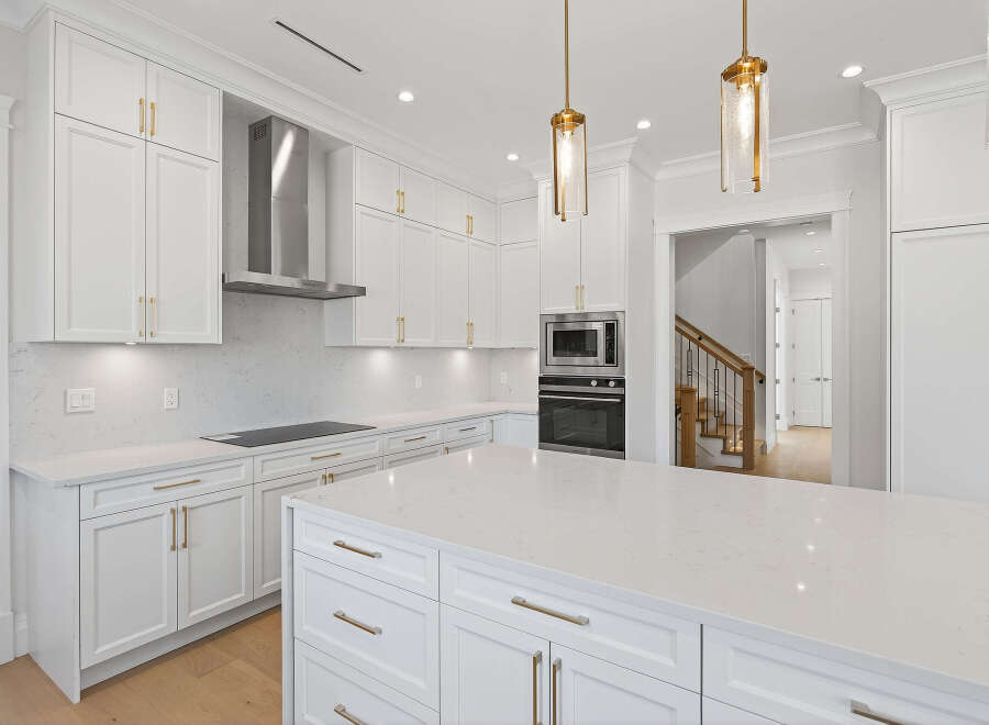 This is a modern kitchen featuring white cabinetry with gold hardware, stainless steel appliances, and a large center island.