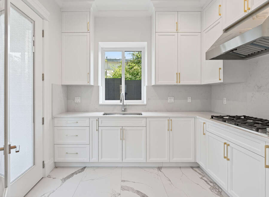 This modern kitchen features sleek, white cabinetry complemented by elegant gold hardware.
