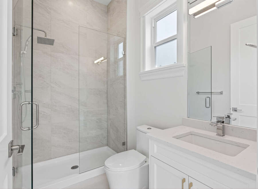This bathroom features a modern design with a walk-in shower enclosed in clear glass, showcasing stylish gray tiling.