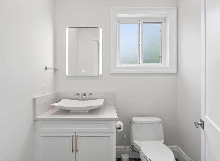 This immaculate, all-white powder room is a vision of modern elegance, featuring a vessel sink atop a stylish vanity.