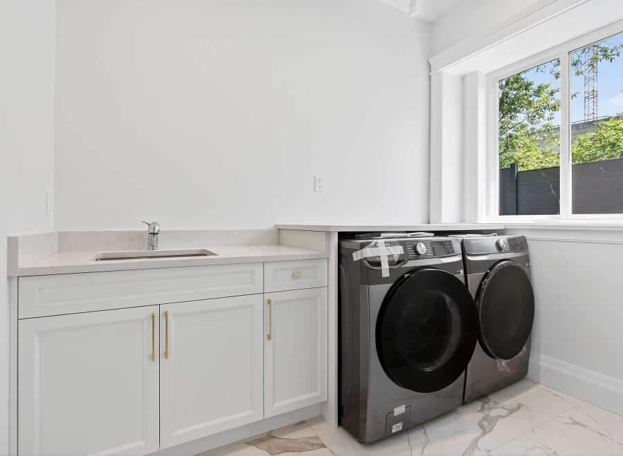 This laundry room features a modern front load washer and dryer set, sleek white cabinetry with gold hardware, and a durable quartz countertop.