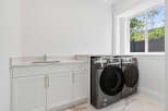 This laundry room features a modern front load washer and dryer set, sleek white cabinetry with gold hardware, and a durable quartz countertop.