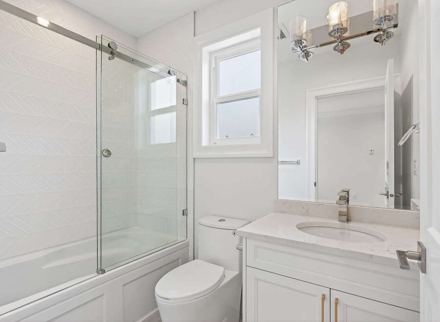 This bright and modern bathroom features a sleek sliding glass shower door, a white vanity with a marble countertop, and a matching toilet.