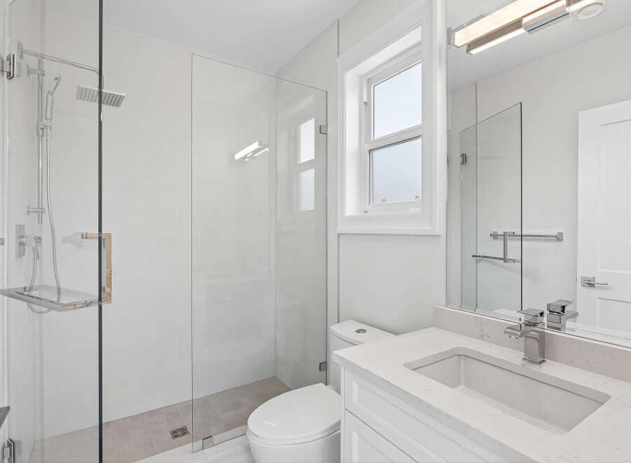 This modern bathroom features a sleek, frameless glass shower with a rainfall showerhead and convenient built-in shelf.