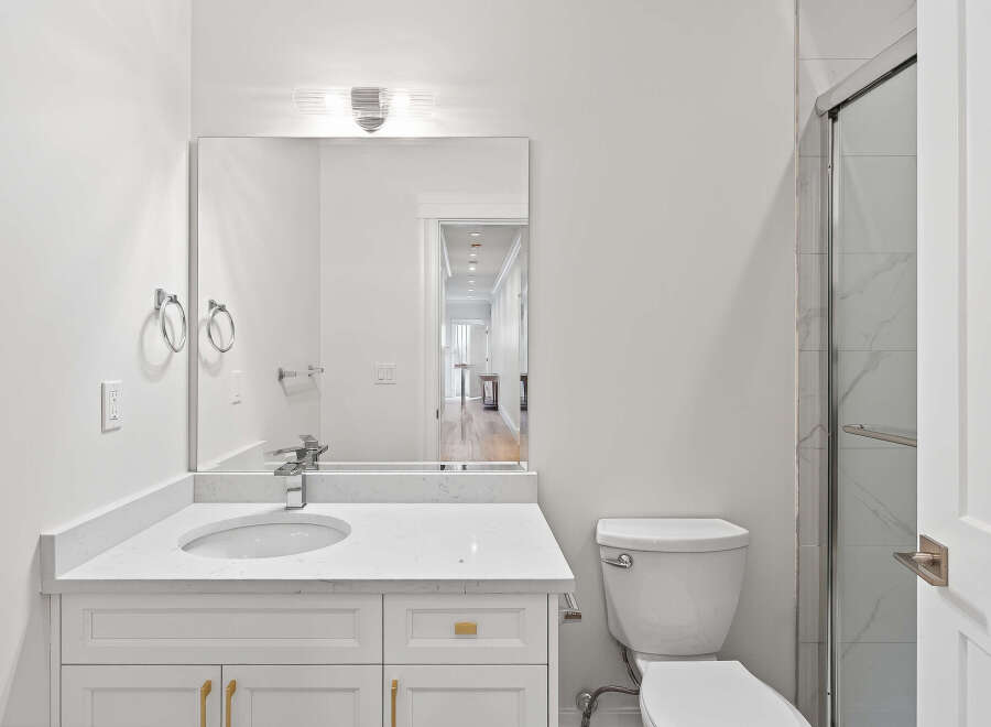 This bright bathroom features a white vanity with gold hardware, a sleek mirror, and a modern toilet.