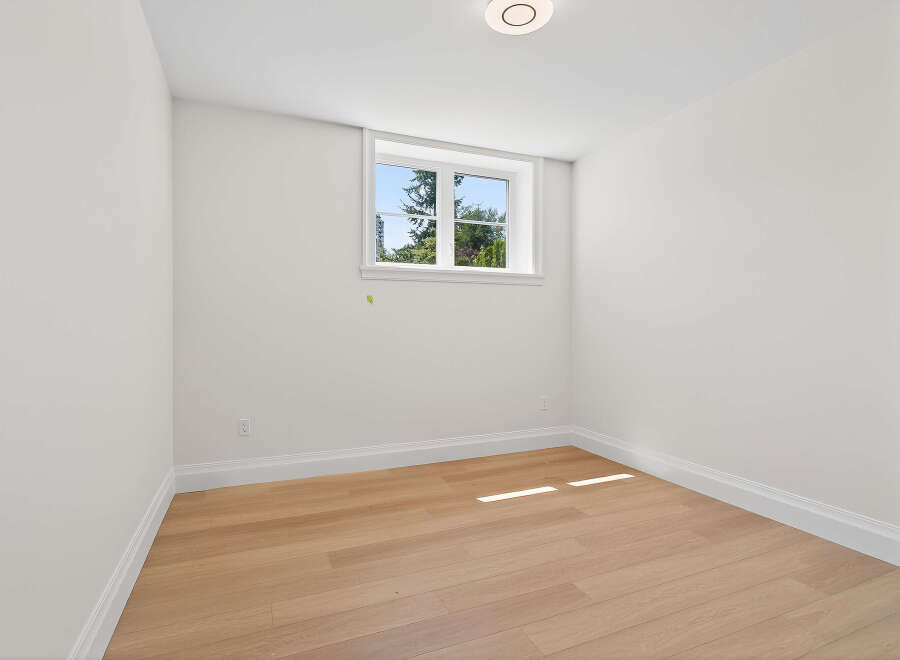 This bright and airy room features pristine white walls, light wood flooring, and a large window offering a view of lush greenery.