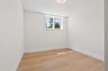 This bright and airy room features pristine white walls, light wood flooring, and a large window offering a view of lush greenery.