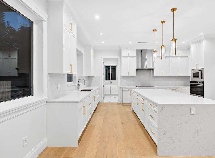 This bright, open-concept kitchen features all-white cabinetry accented with gold hardware, creating a luxurious and modern feel.