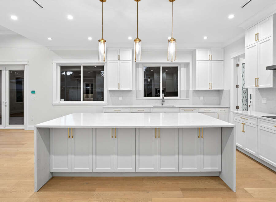 This modern kitchen features sleek white cabinetry with gold hardware, a spacious island with a quartz countertop, and stylish pendant lighting.