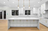 This modern kitchen features sleek white cabinetry with gold hardware, a spacious island with a quartz countertop, and stylish pendant lighting.