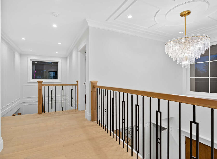 This interior showcases a luxurious hallway with light hardwood floors, leading to a staircase with an elegant black metal railing.