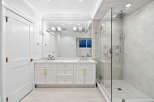 This is a bright and modern bathroom featuring a double vanity with gold hardware, a spacious walk-in shower with gray marble-style tiling and a rainfall showerhead.