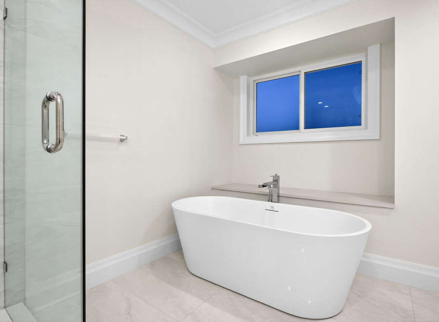 Indulge in the tranquility of this bathroom featuring a sleek, freestanding tub positioned beneath a window offering natural light.