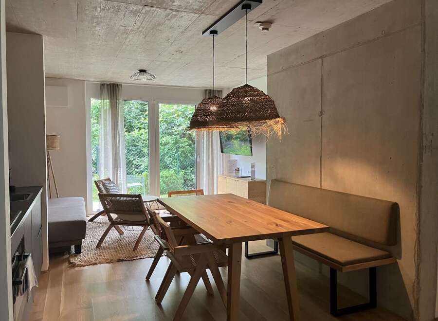 This inviting living space features a solid wood dining table illuminated by stylish woven pendant lights, complemented by a cozy built-in bench and woven chairs.