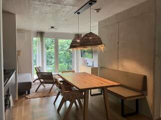 This inviting living space features a solid wood dining table illuminated by stylish woven pendant lights, complemented by a cozy built-in bench and woven chairs.