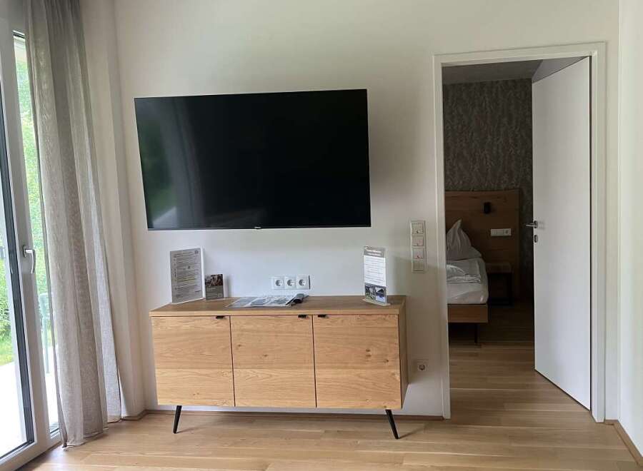 This is a bright and modern hotel room featuring a flat-screen TV mounted above a wooden cabinet.