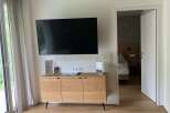This is a bright and modern hotel room featuring a flat-screen TV mounted above a wooden cabinet.
